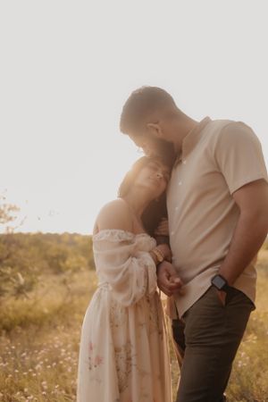 Couple in casual attire sharing intimate moment in golden field at sunset.