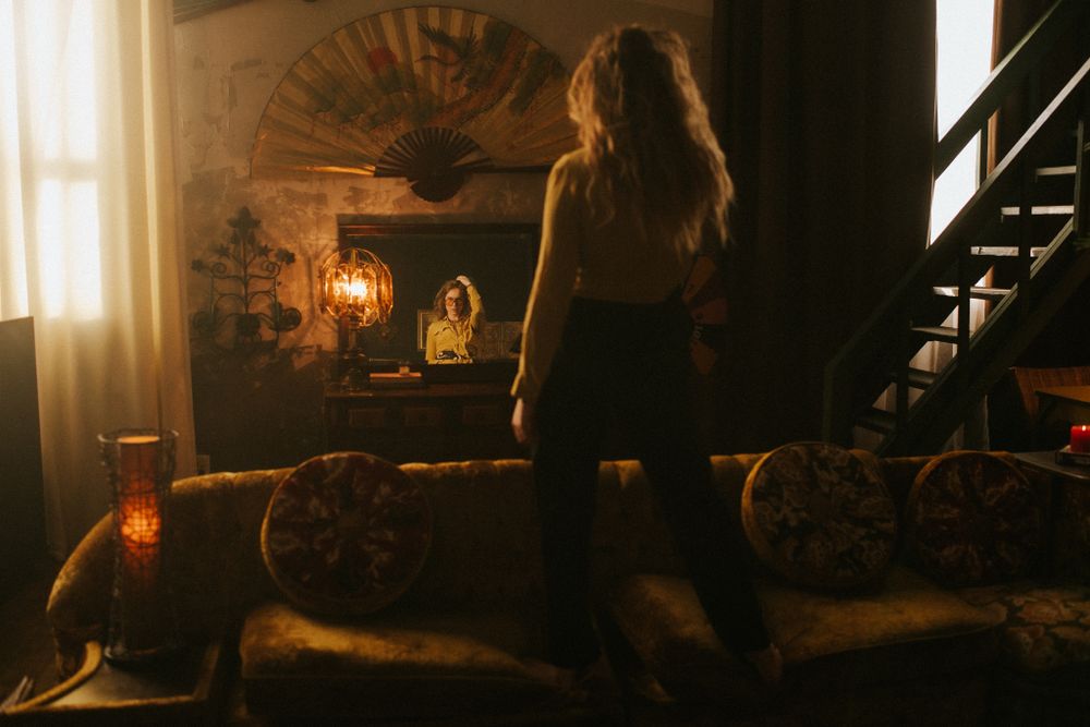 Skye Wallace stands in an warm living room setting looking into a mirror
