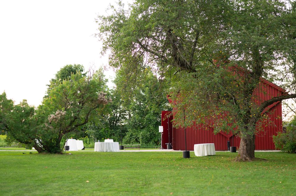 Red barn and white tent set up on lush green lawn for outdoor wedding celebration.