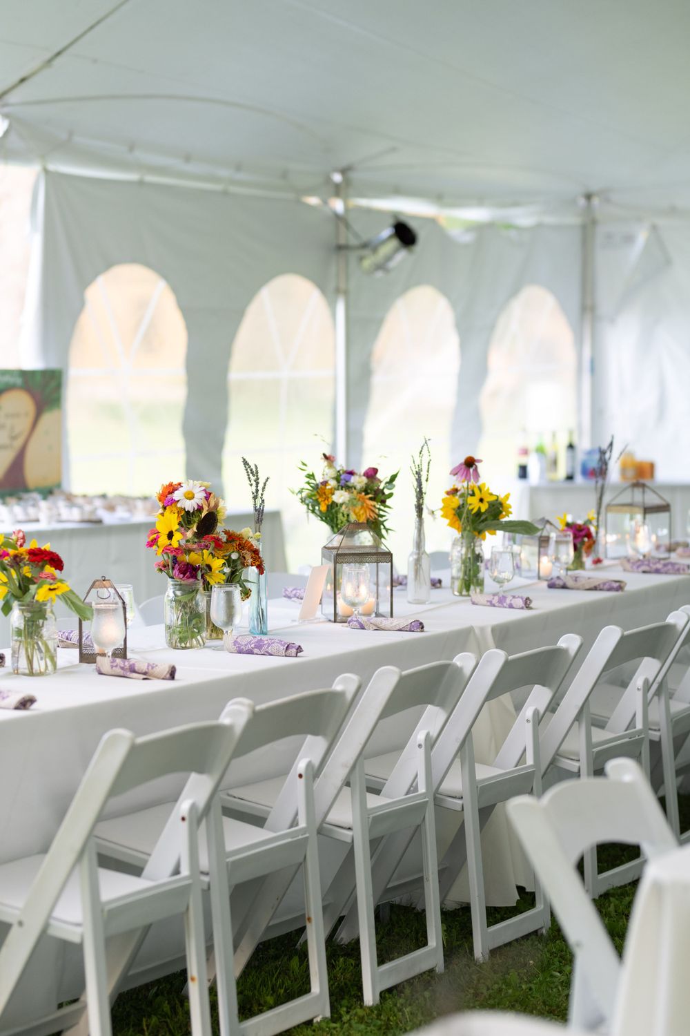 White wedding reception tent with decorated tables featuring colorful floral centerpieces and elegant place settings.