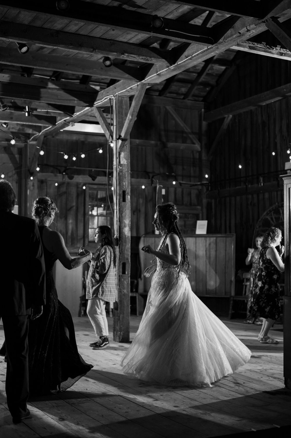 Dancing under string lights in a rustic barn venue during a wedding celebration.