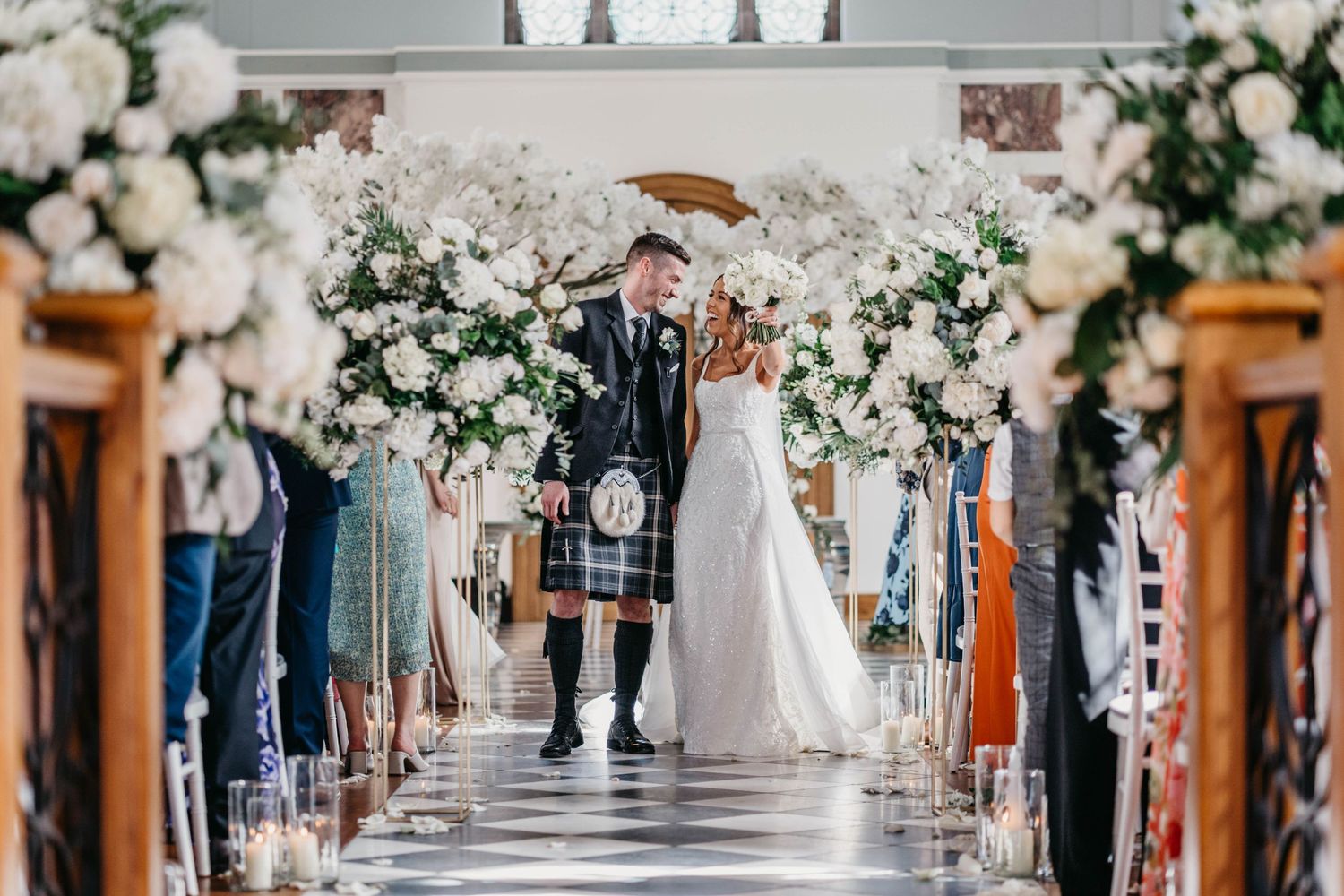 Wedding ceremony aisle decorated with elegant white floral arrangements and wooden accents.
