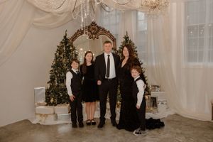 Elegant family portrait in front of decorated Christmas trees and ornate mirror.