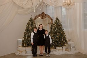 Family group photo with Christmas trees and ornate mirror in elegant white room.