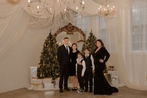 Holiday family portrait with decorated Christmas trees and elegant white draping.