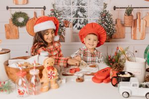 Children wearing holiday hats and baking cookies together amid Christmas kitchen decorations.