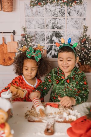 Children in holiday attire decorating Christmas cookies together at a festive table.