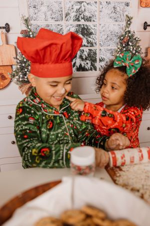 Two children in holiday attire baking Christmas cookies together in a festive kitchen setting.
