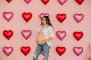 Valentine's themed maternity photo against pink background with heart balloons.