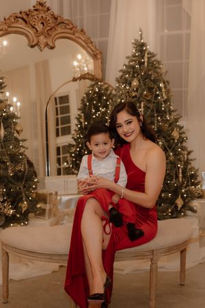 An elegant holiday portrait session with decorated Christmas trees and a vintage mirror backdrop.