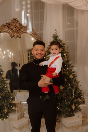 A festive holiday portrait in front of decorated Christmas trees and an ornate mirror.