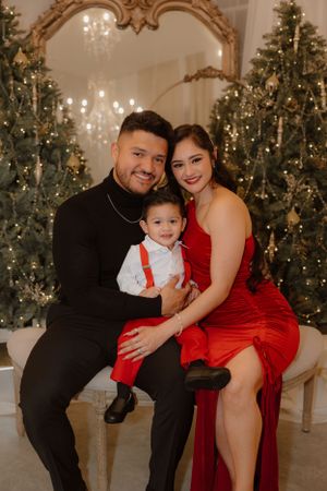 A family poses in front of decorated Christmas trees wearing formal attire in a holiday photo session.