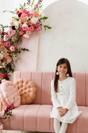 Interior photo featuring pink velvet couch with lush floral arrangement in archway.
