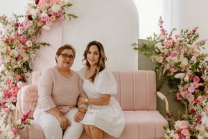 Two people sitting on pink couch surrounded by elegant floral arrangements.