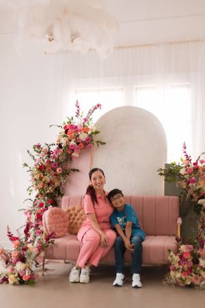 Modern studio setup with pink couch, floral arrangements and arched backdrop.