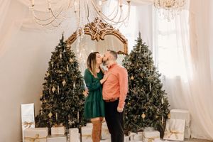 Couple shares romantic moment in front of decorated Christmas trees and ornate mirror.