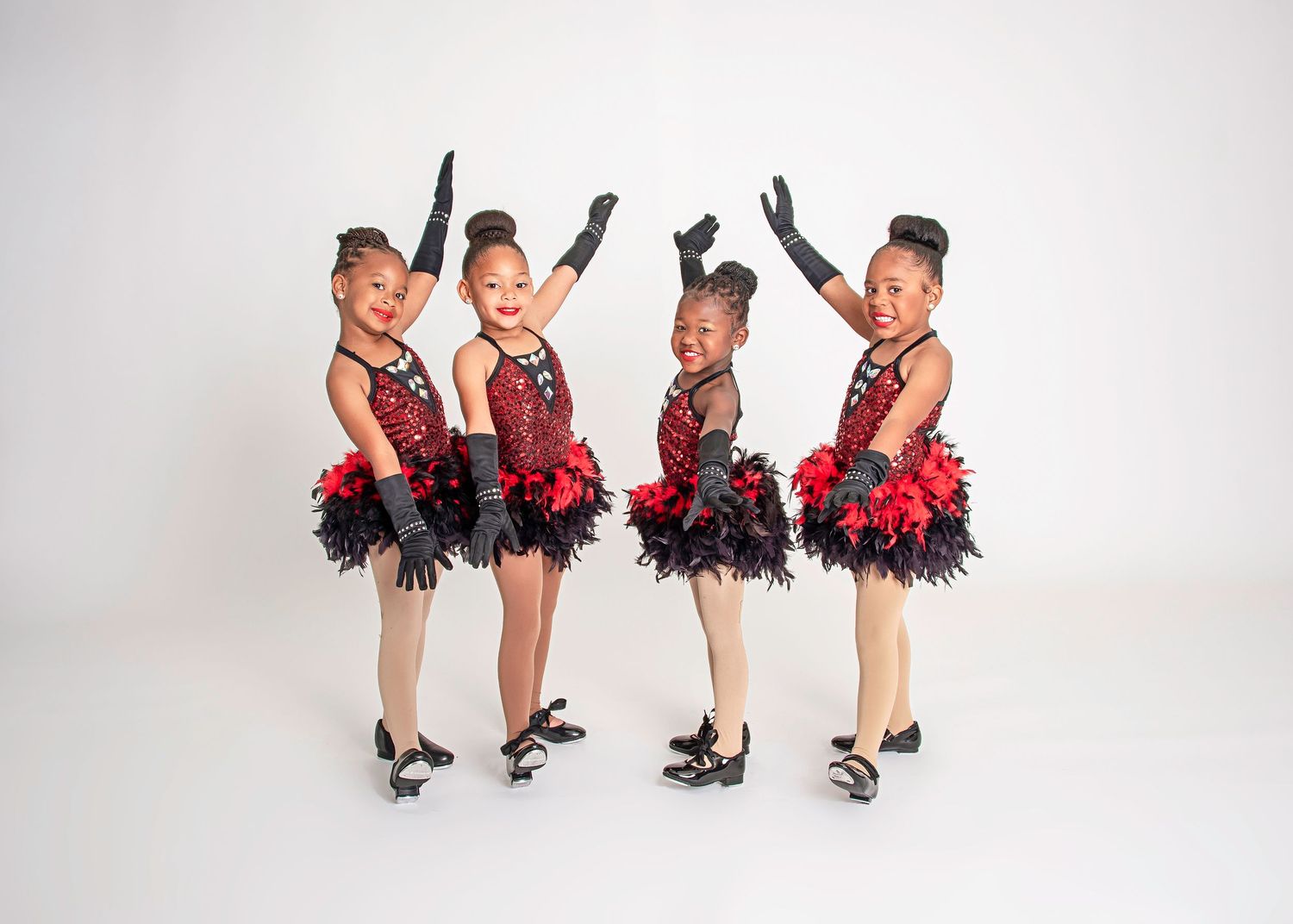 Four young dancers in matching red and black performance costumes striking poses.