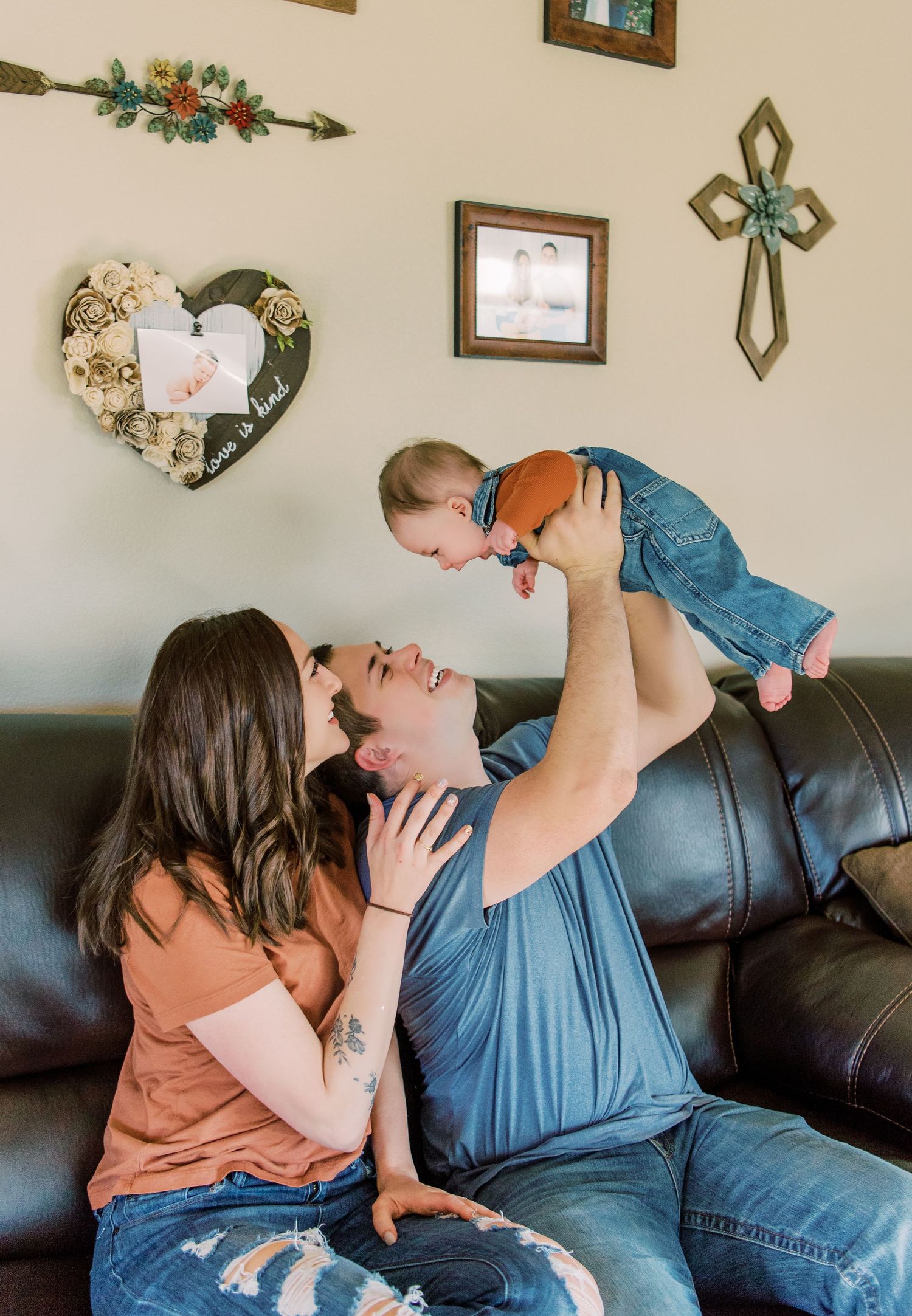 A heartwarming family moment on a leather couch with decorative wall art including a heart and cross in the background.