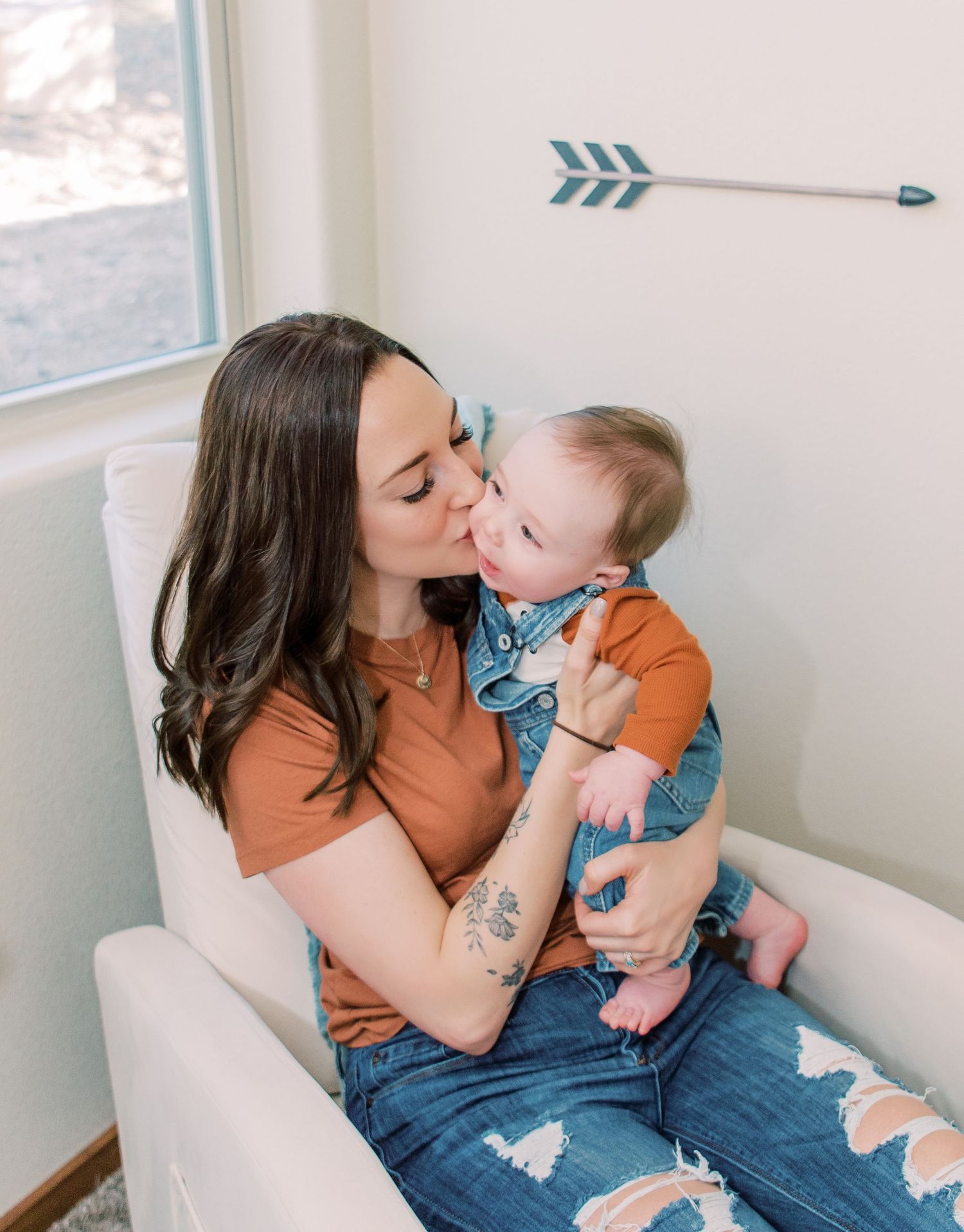 A tender moment shared between a parent and baby while sitting in a white chair near a wall decorated with an arrow.
