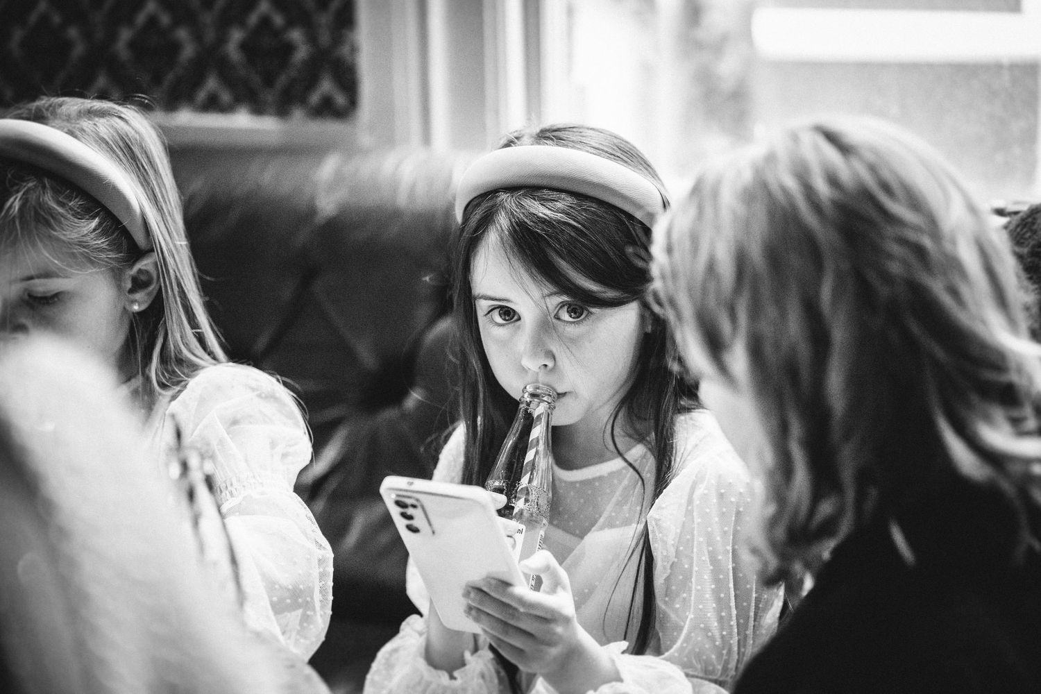 A child sips through a straw while sitting on leather seating with patterned wallpaper behind.