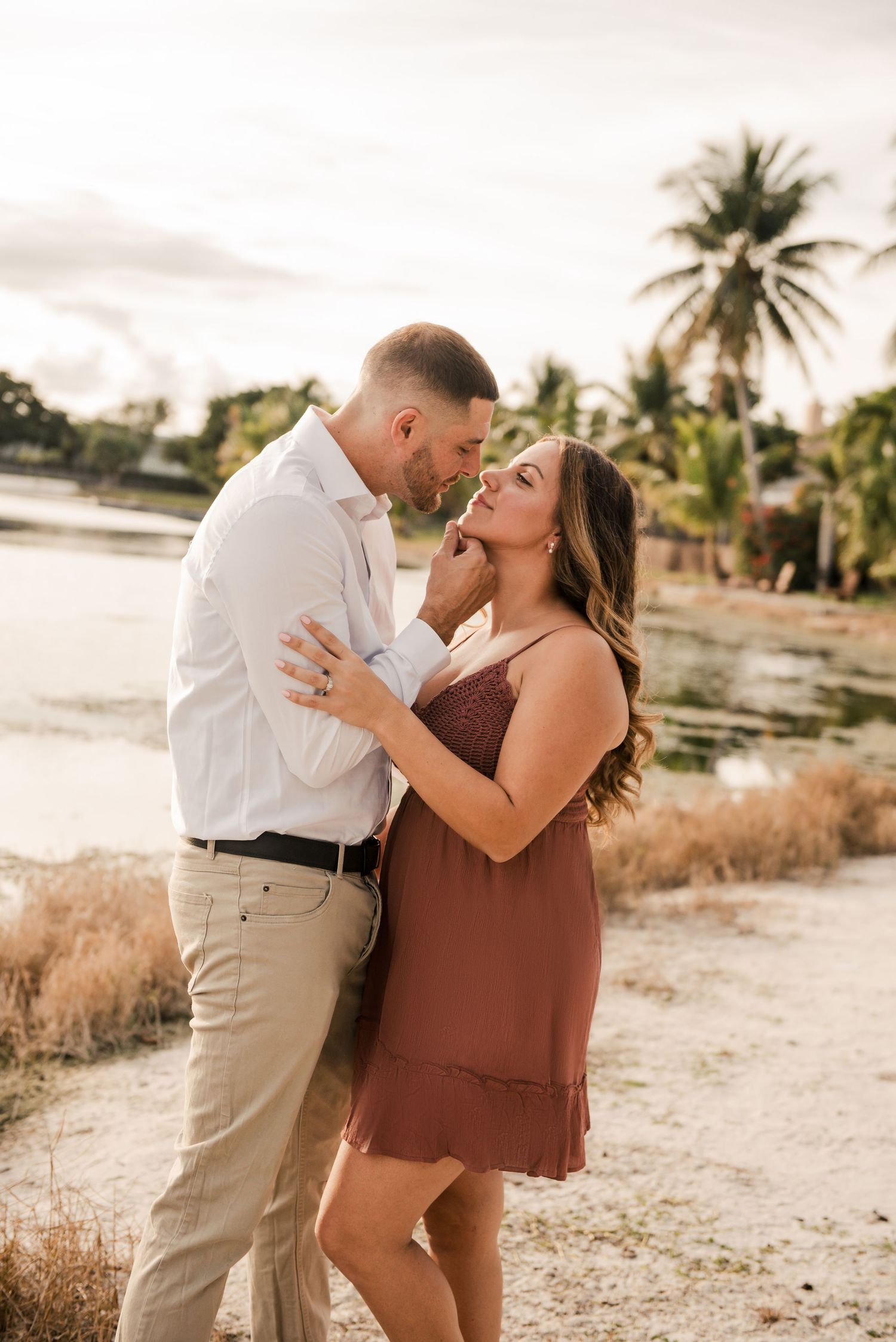 A romantic sunset engagement photoshoot on a beach with palm trees and golden light.