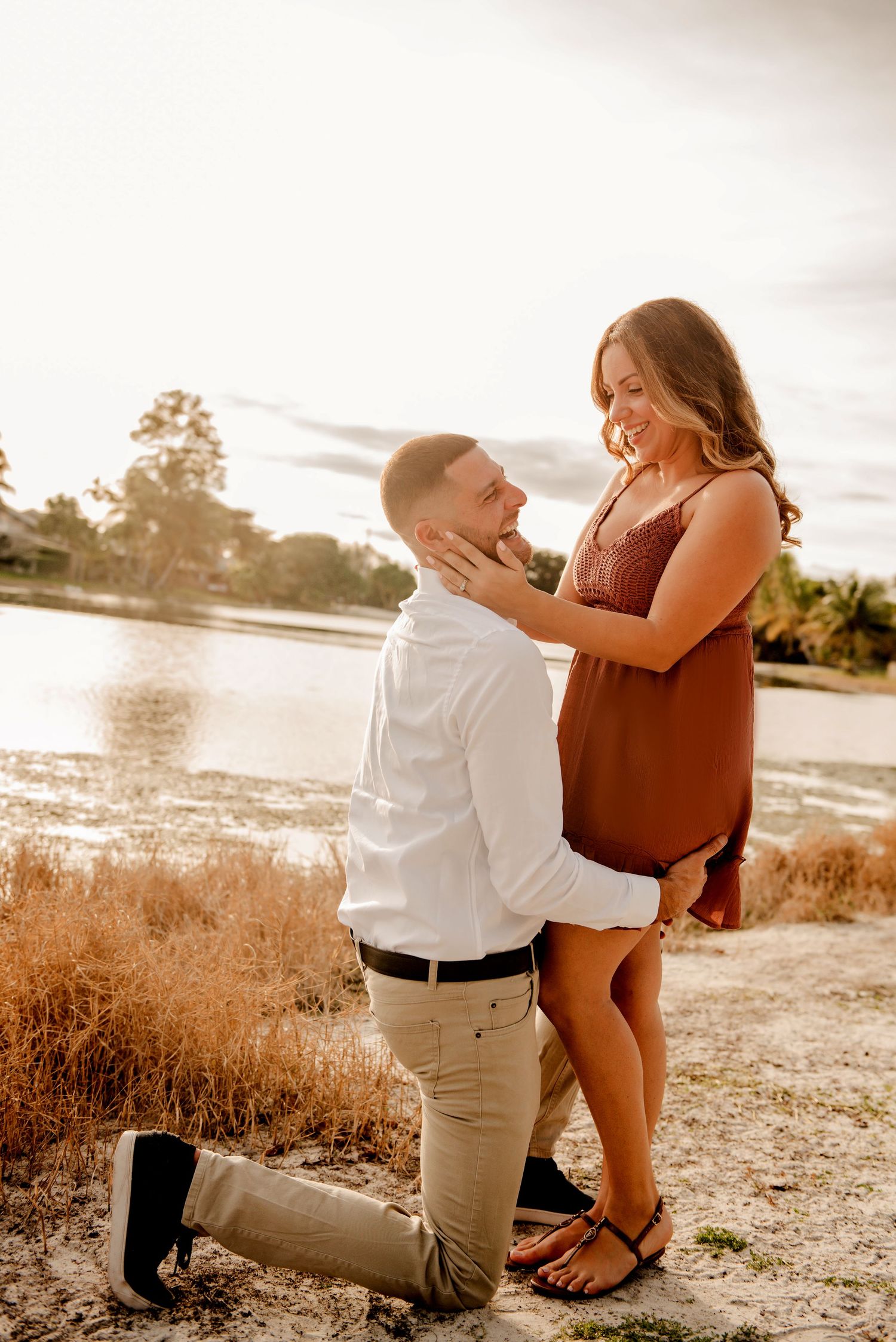 A romantic proposal moment captured at sunset by a lake with the couple sharing an emotional embrace.