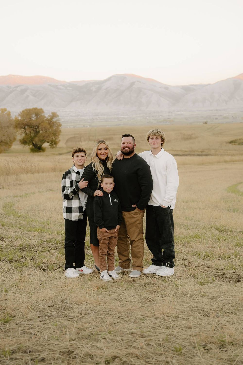 Family portrait in casual wear against mountain landscape backdrop.