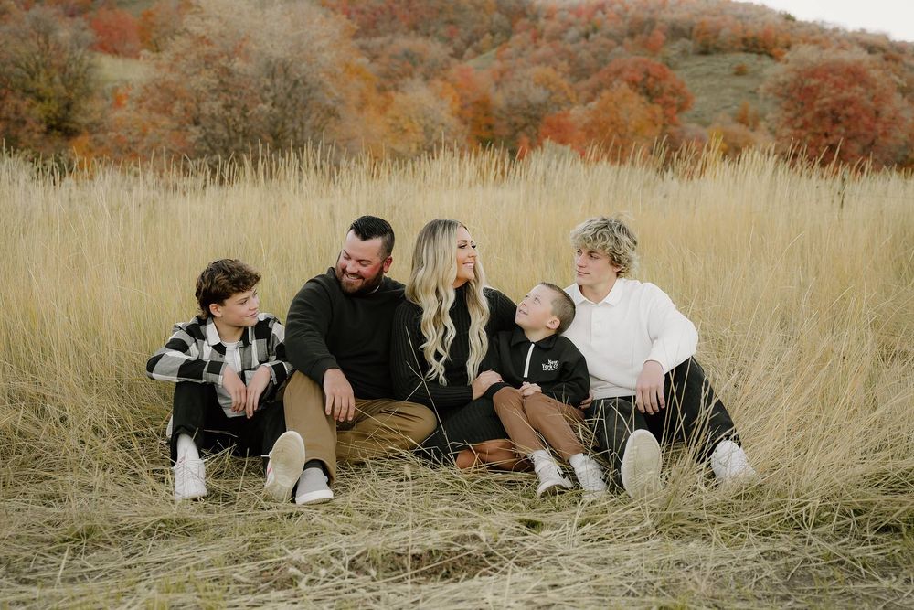 Family sitting together in tall grass field with mountain backdrop.