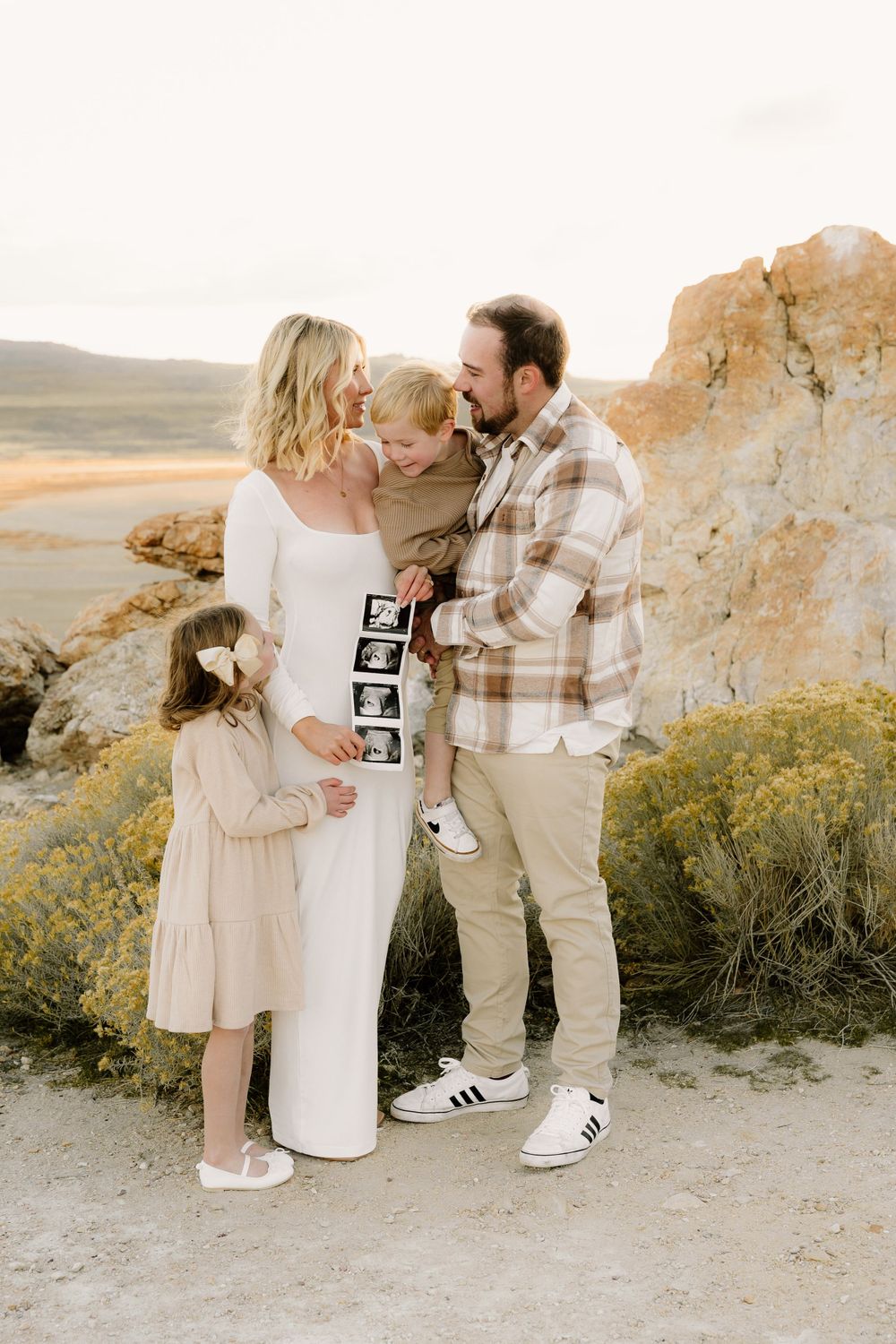 Family with children posing in front of rocky landscape while sharing pregnancy announcement photos.