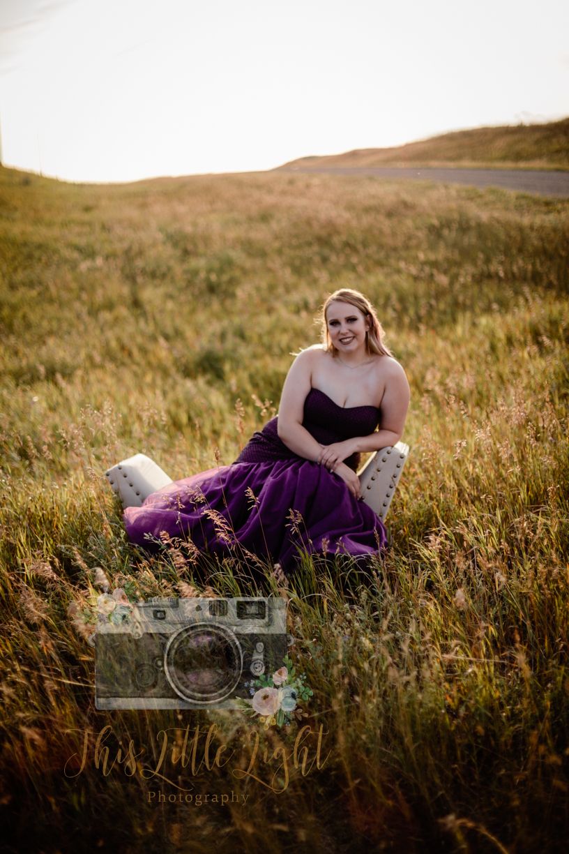Young woman in purple gown sitting in chair in golden meadow at sunset. Senior grad photos. Graduation photos.