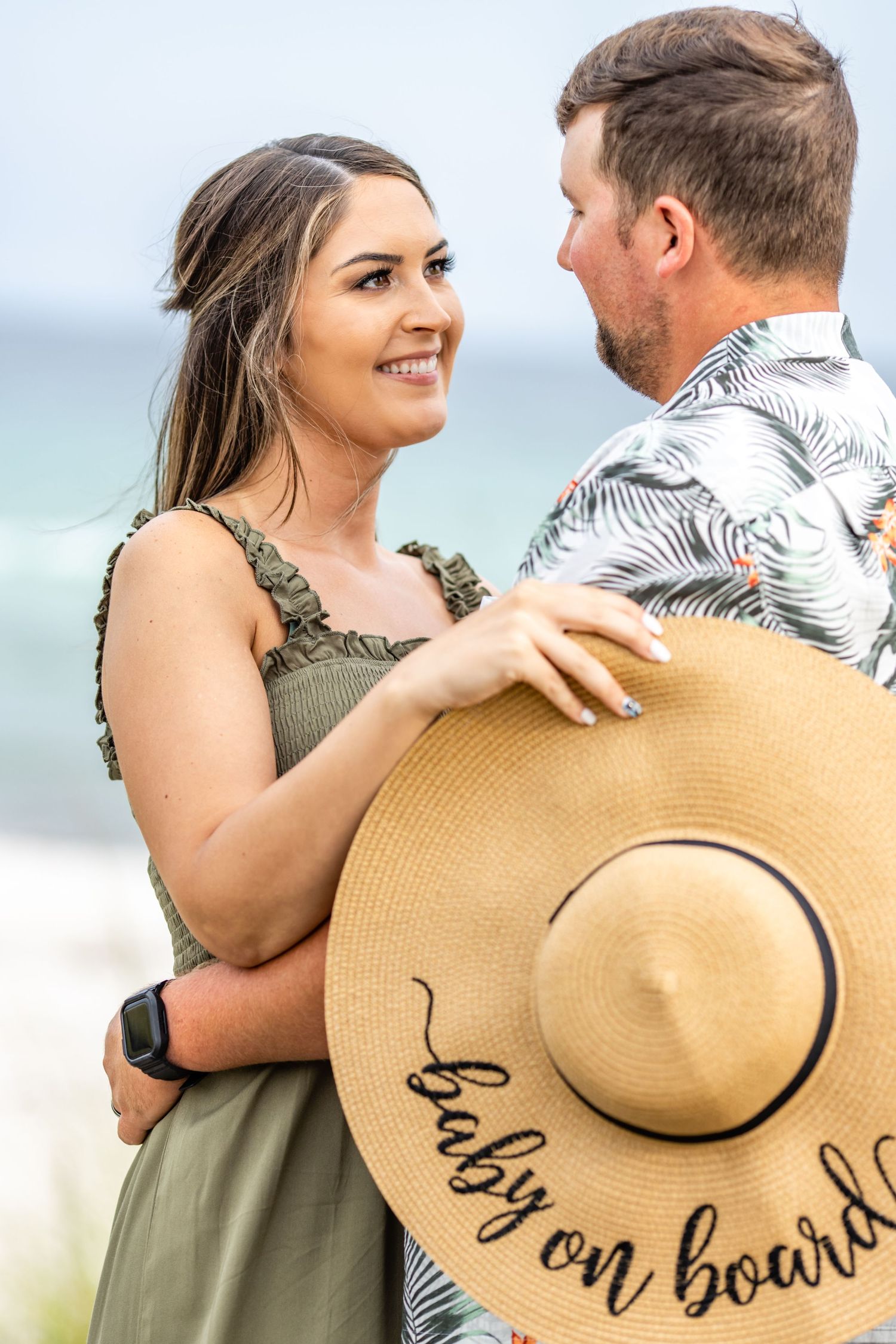 A couple shares an intimate moment on the beach with a decorative sun hat.