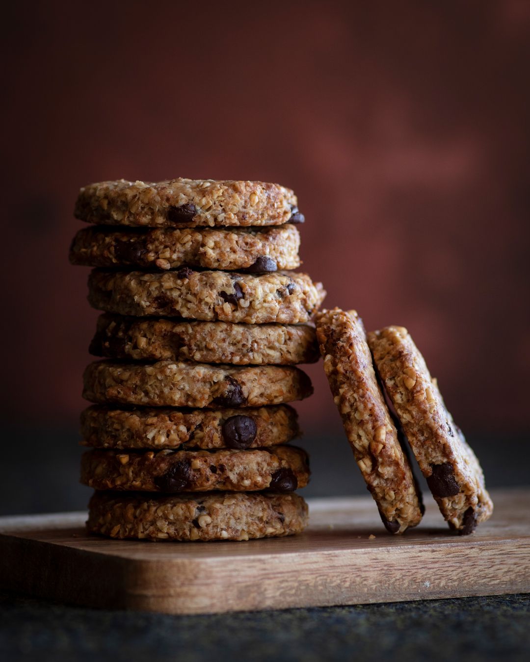 Stacks of homemade chocolate oatmeal cookies on a rustic wooden board against a dark moody background.