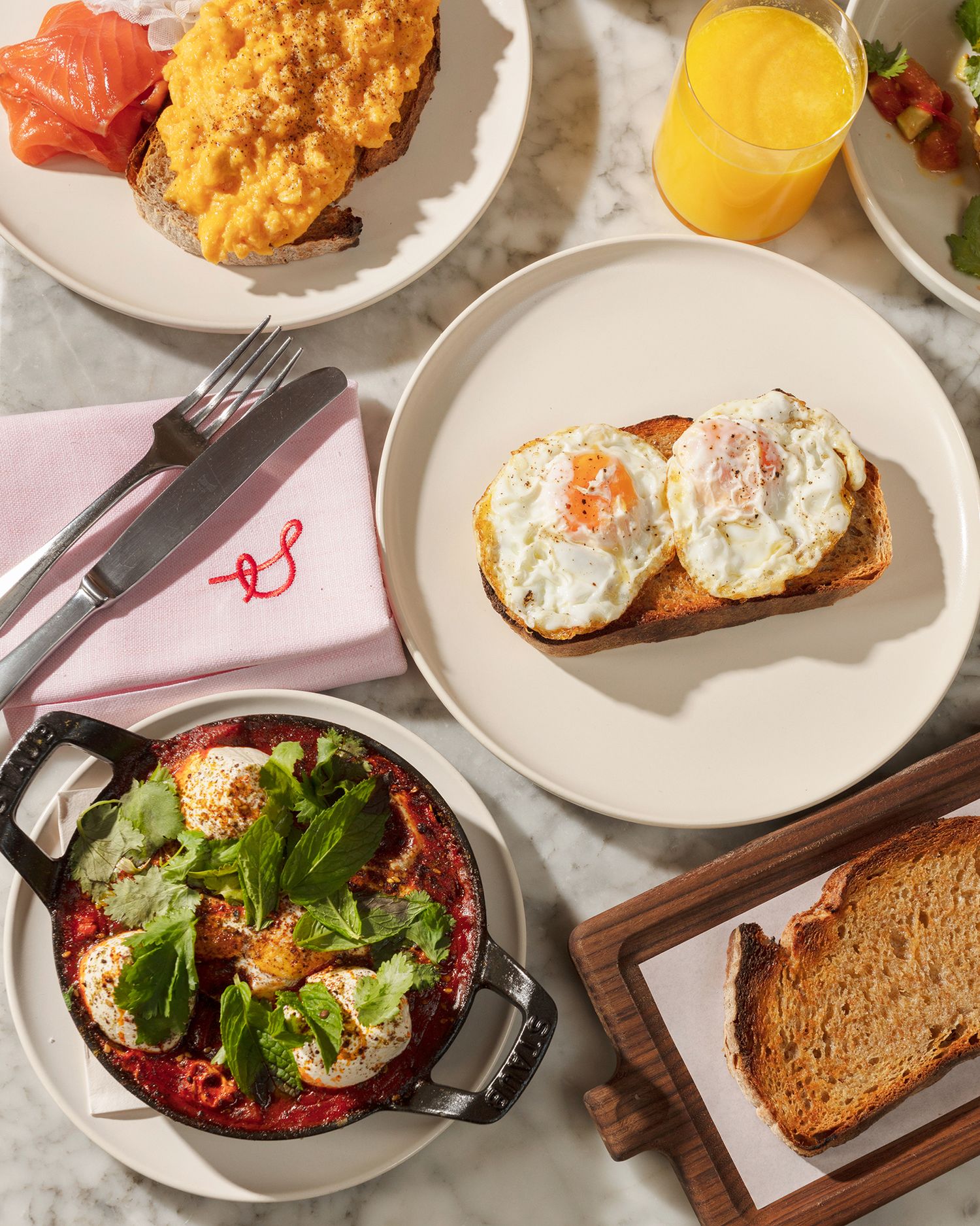 A breakfast spread featuring eggs on toast, orange juice, and a side dish served in a rustic cast iron skillet.