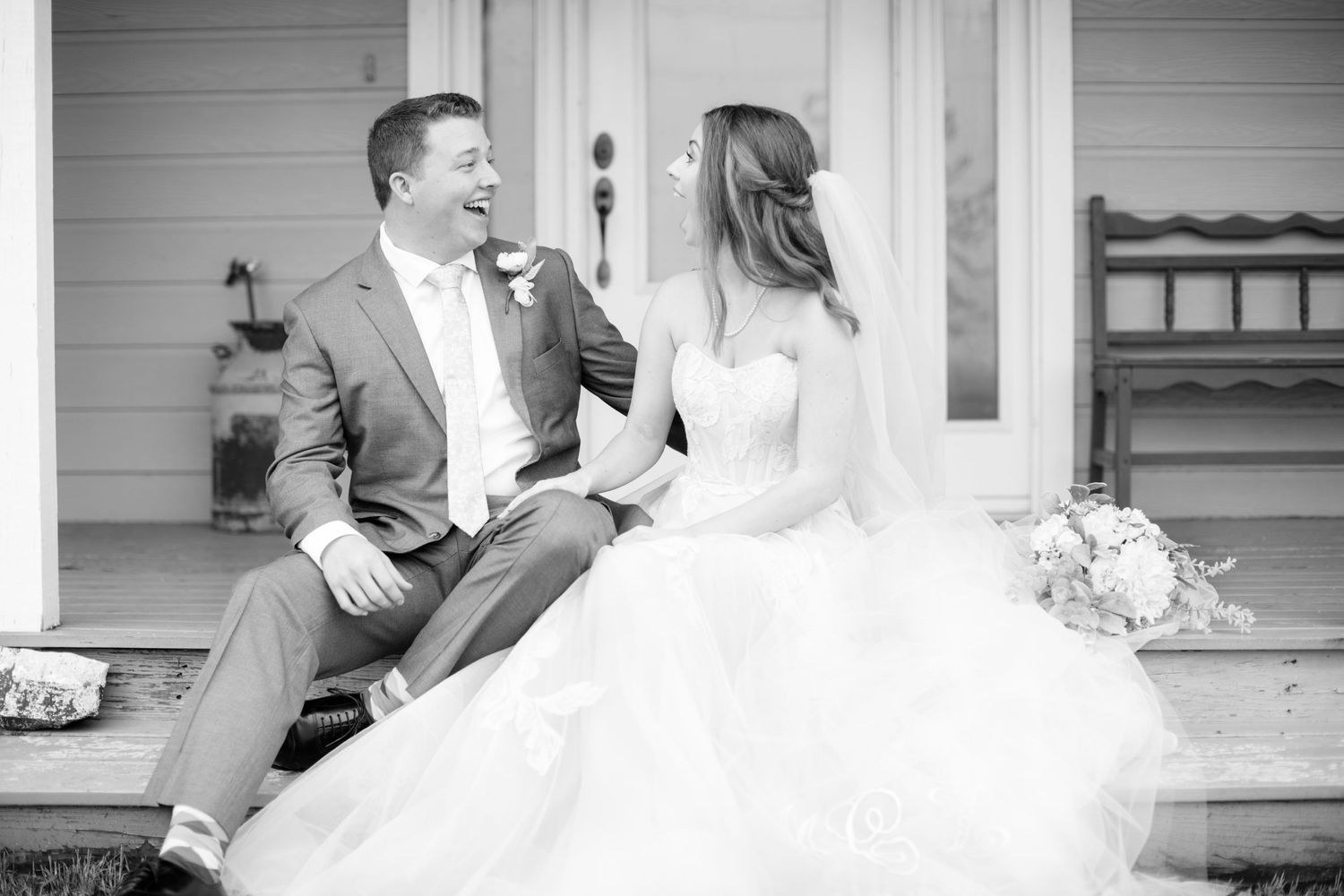 Candid moment of newlyweds laughing together on porch steps.