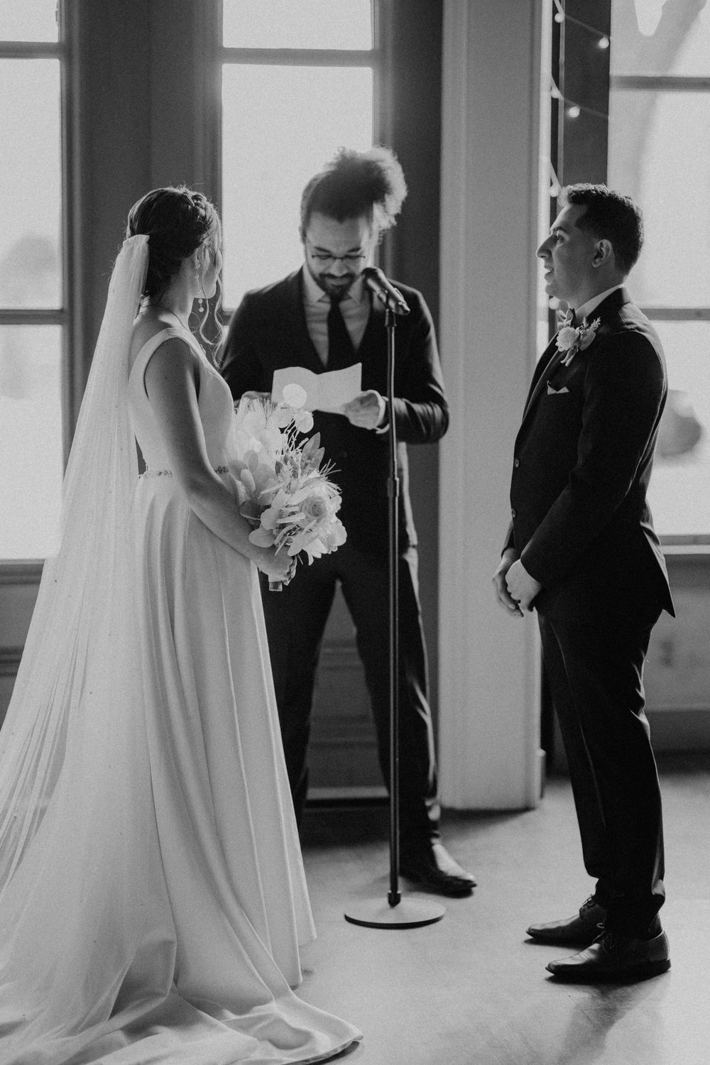 Black and white photo of officiant reading vows at elegant indoor wedding ceremony.