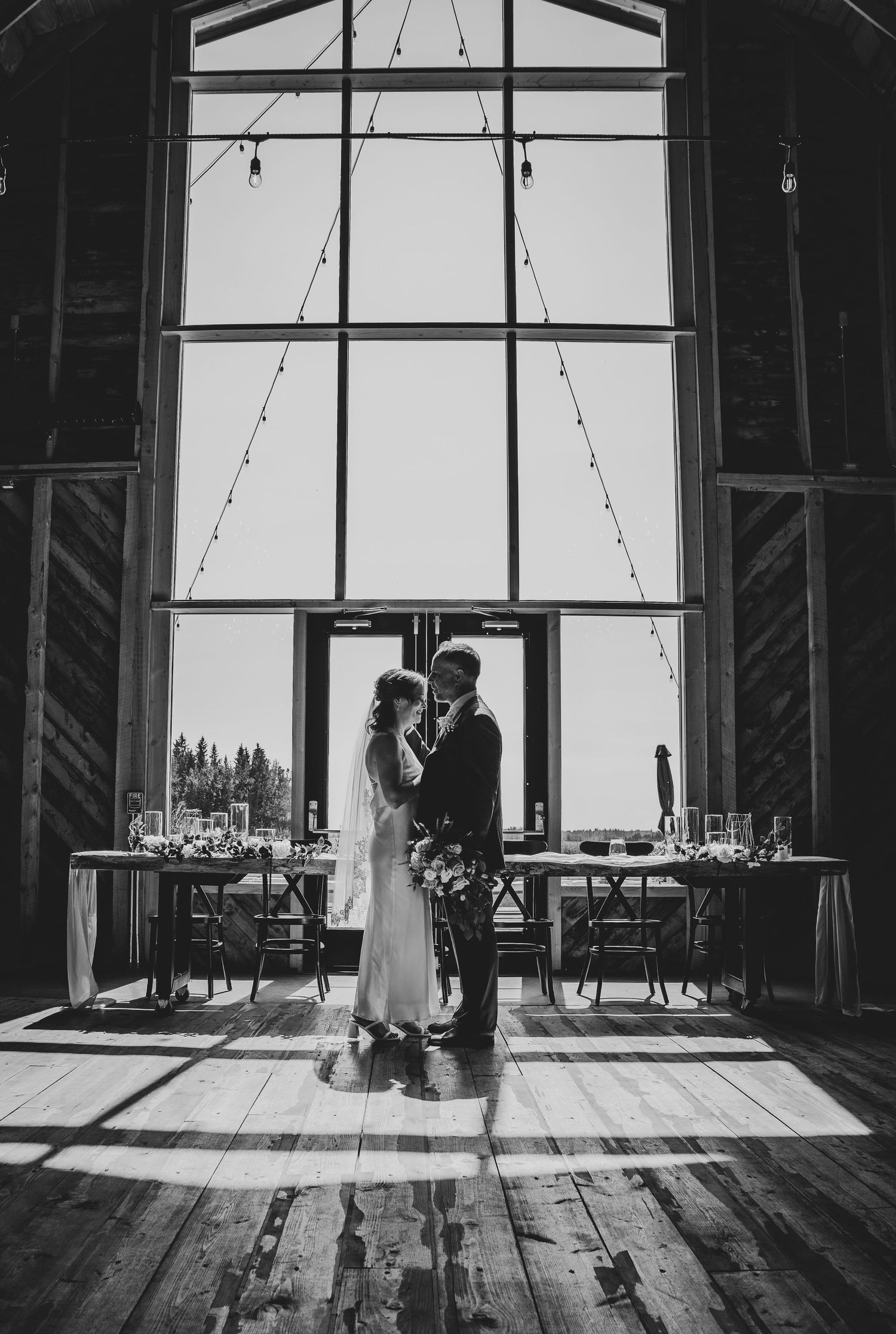 Silhouetted figures in rustic barn venue with dramatic window lighting and string lights.
