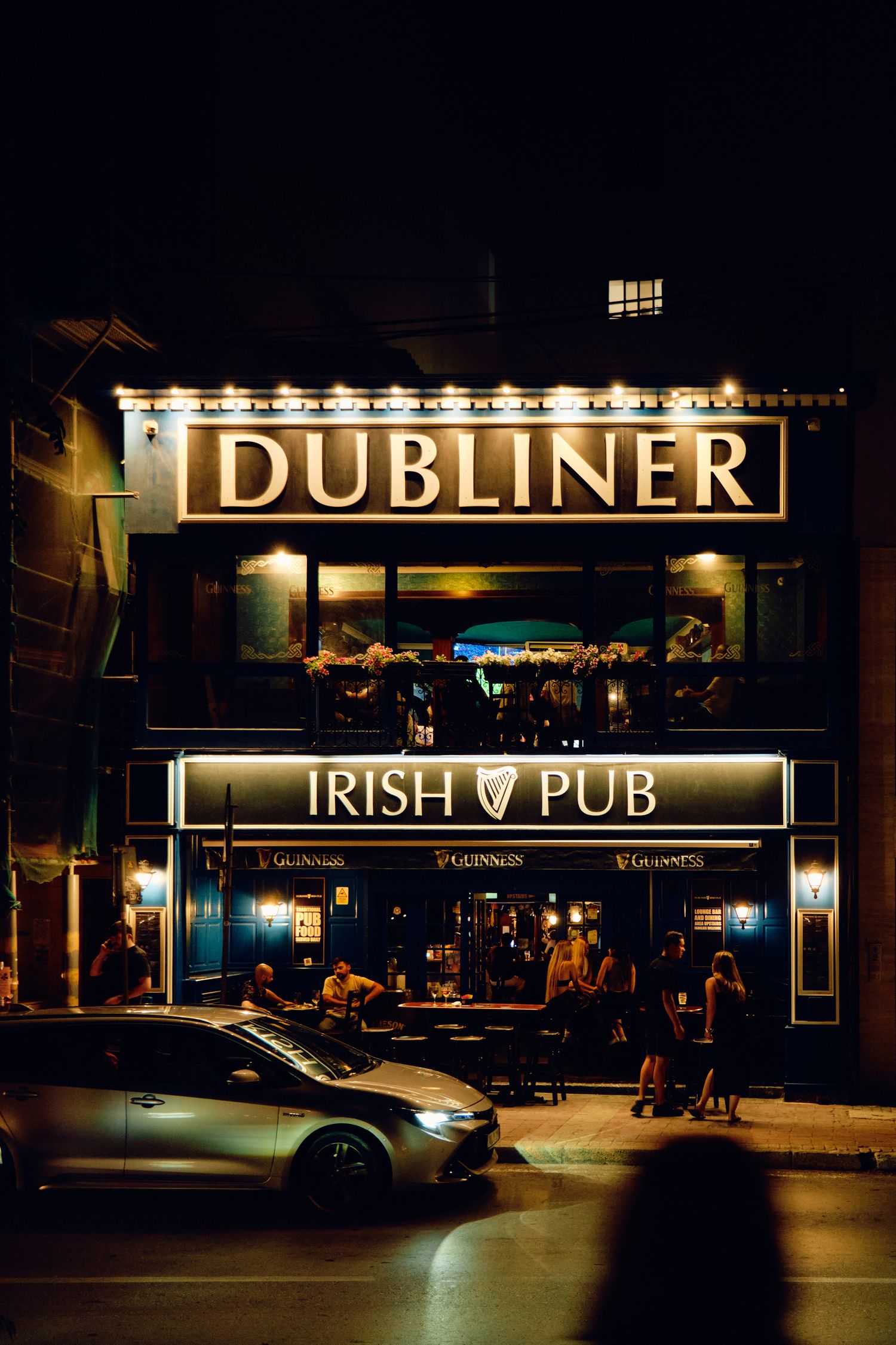 Illuminated Dubliner Irish Pub storefront at night with glowing signage and parked car.