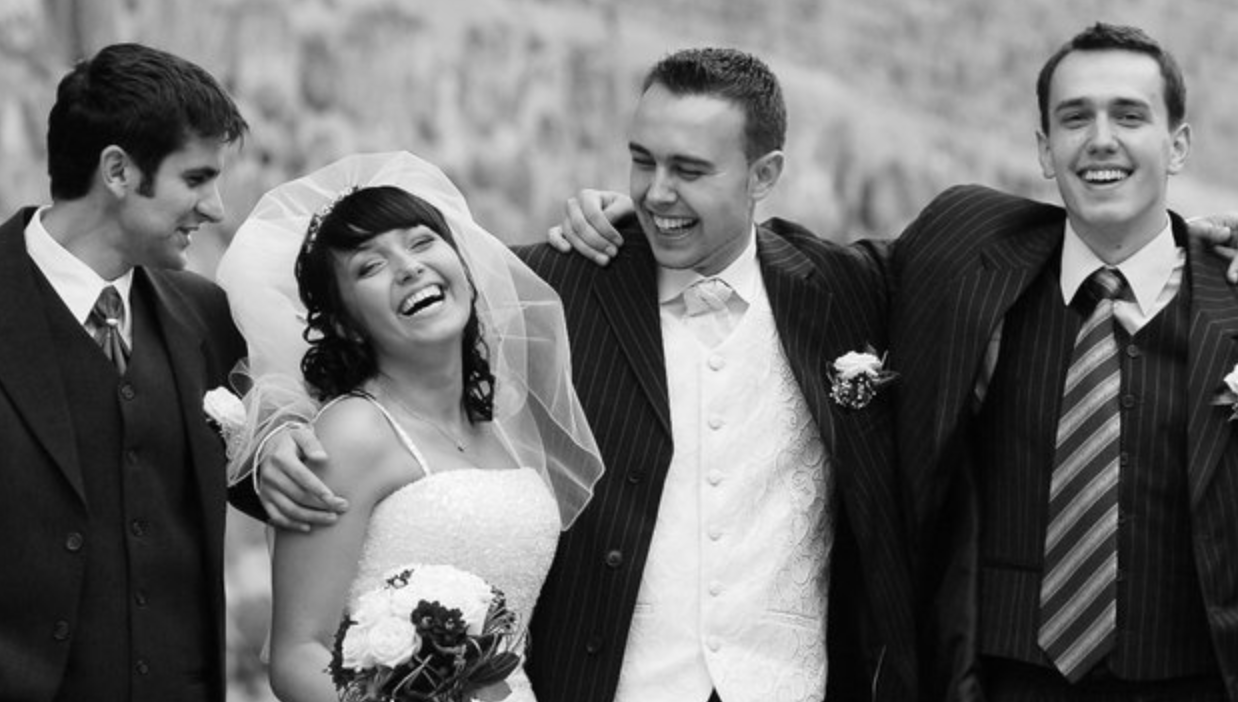 A vintage black and white wedding photograph showing a group celebrating with joyful expressions.