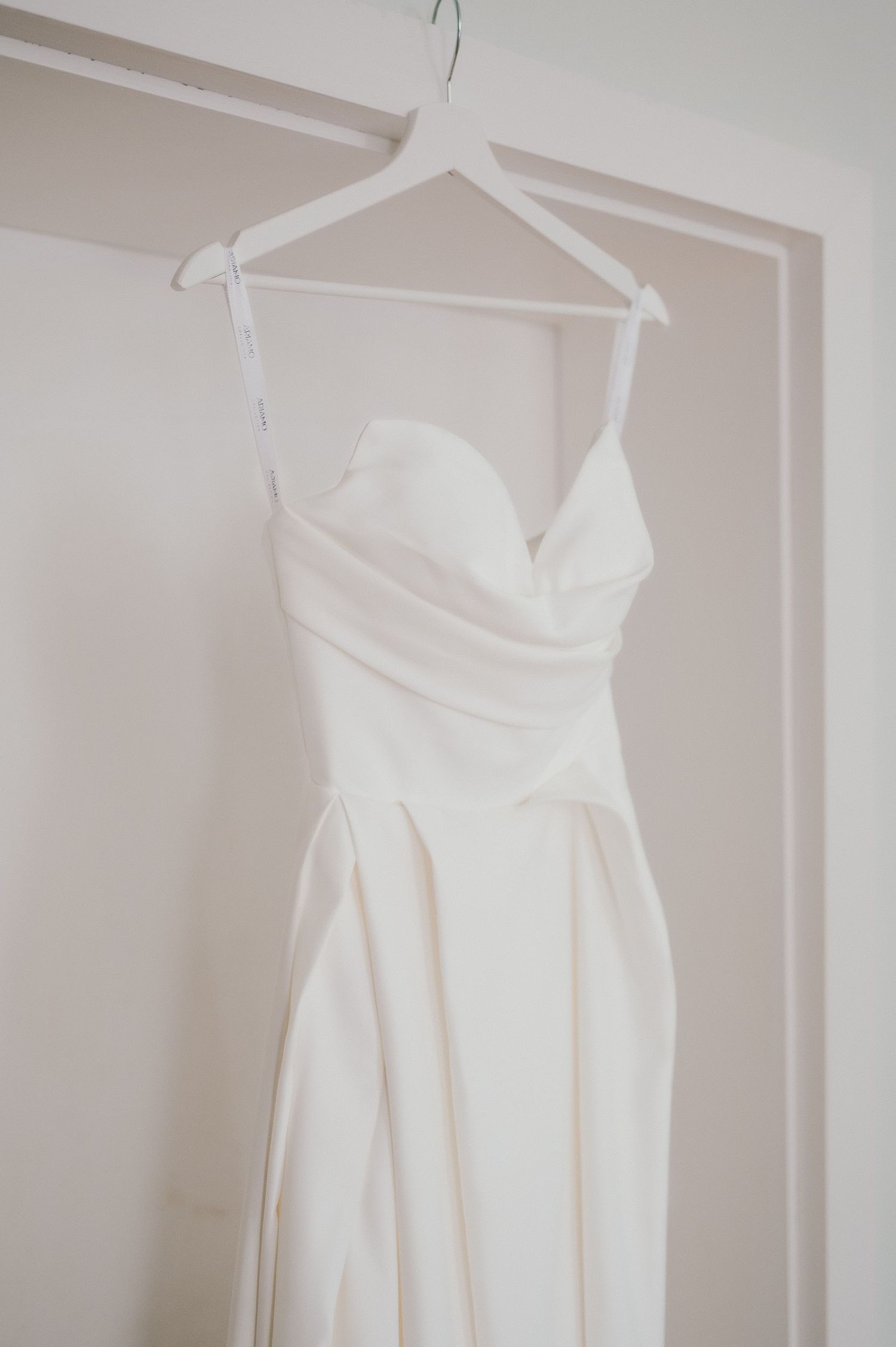 A white wedding dress with sweetheart neckline hangs on display against a neutral wall.