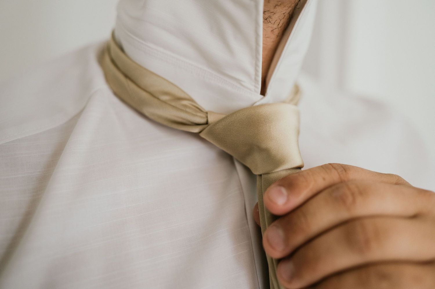 Close-up of hands adjusting champagne colored tie against white formal shirt.