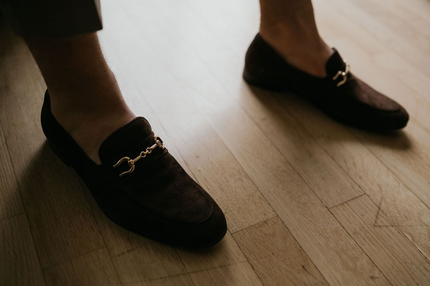 Black leather loafers with gold hardware details on hardwood flooring.