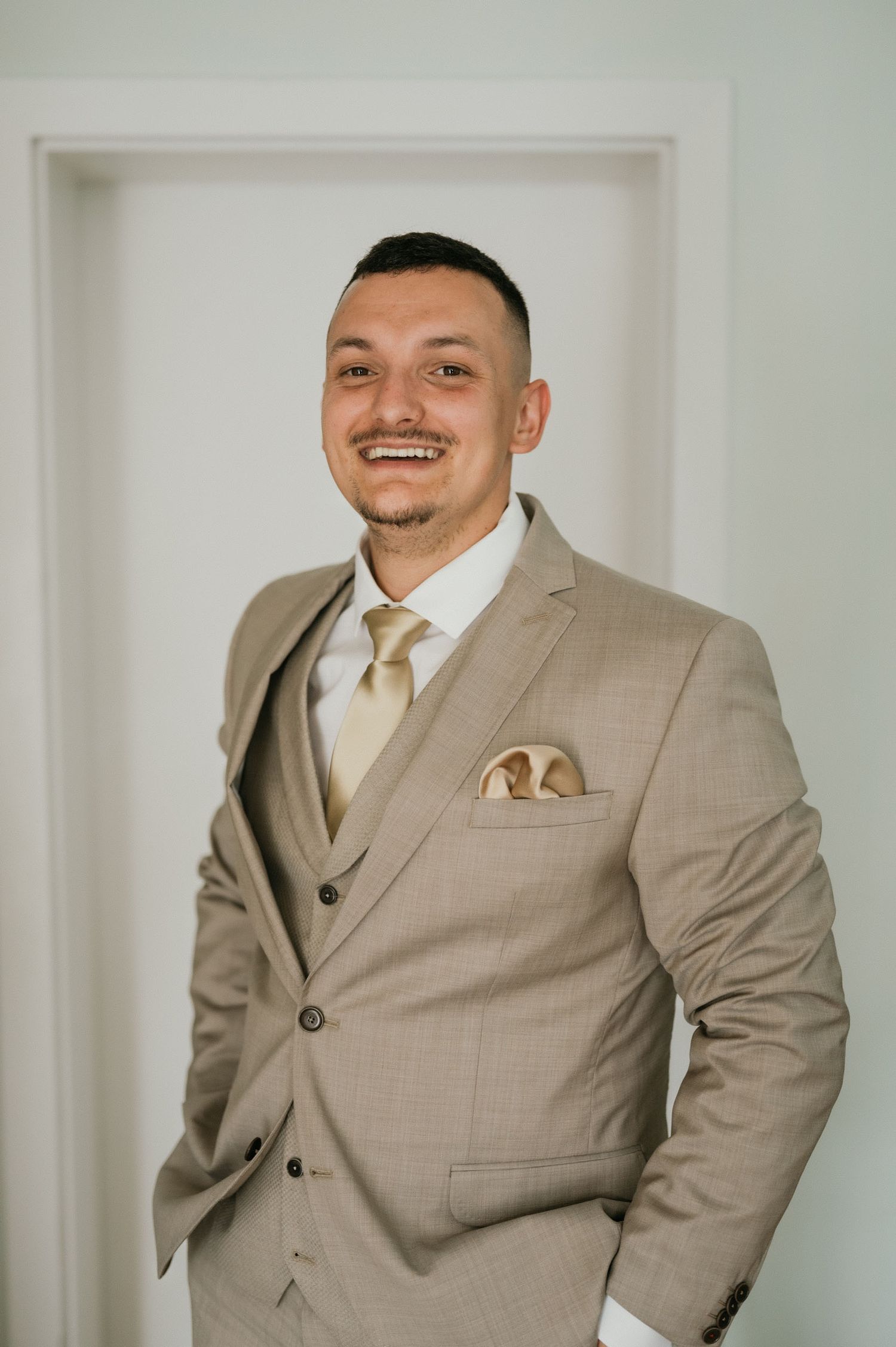 A formal three-piece tan suit with matching tie and decorative pocket square in an elegant pose.