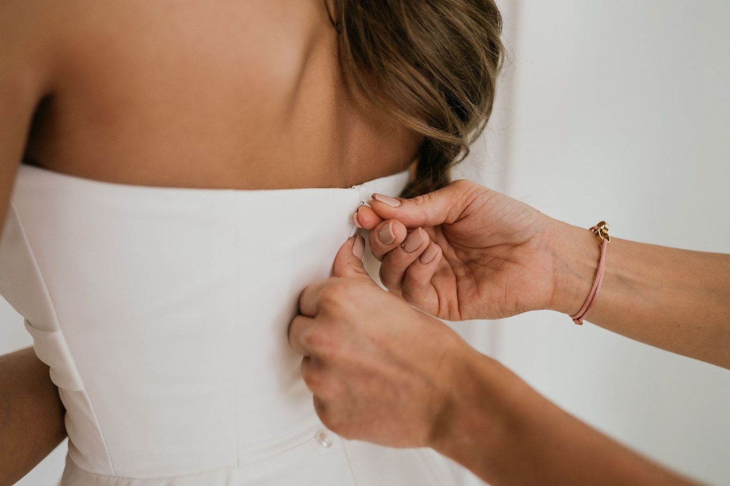 Hands helping to fasten the back of a white wedding dress.