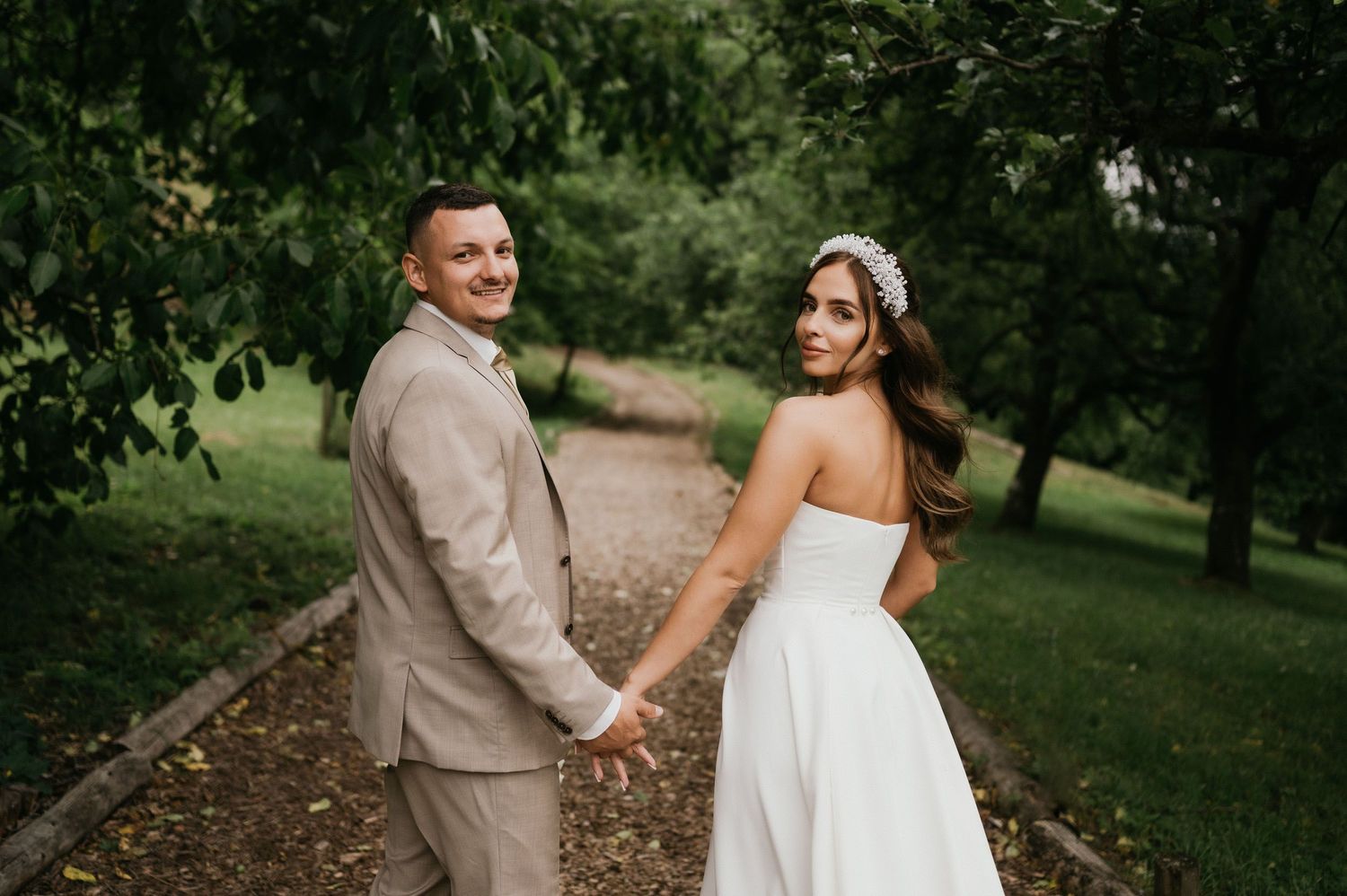 Couple holding hands while walking on a garden path, looking back at camera.