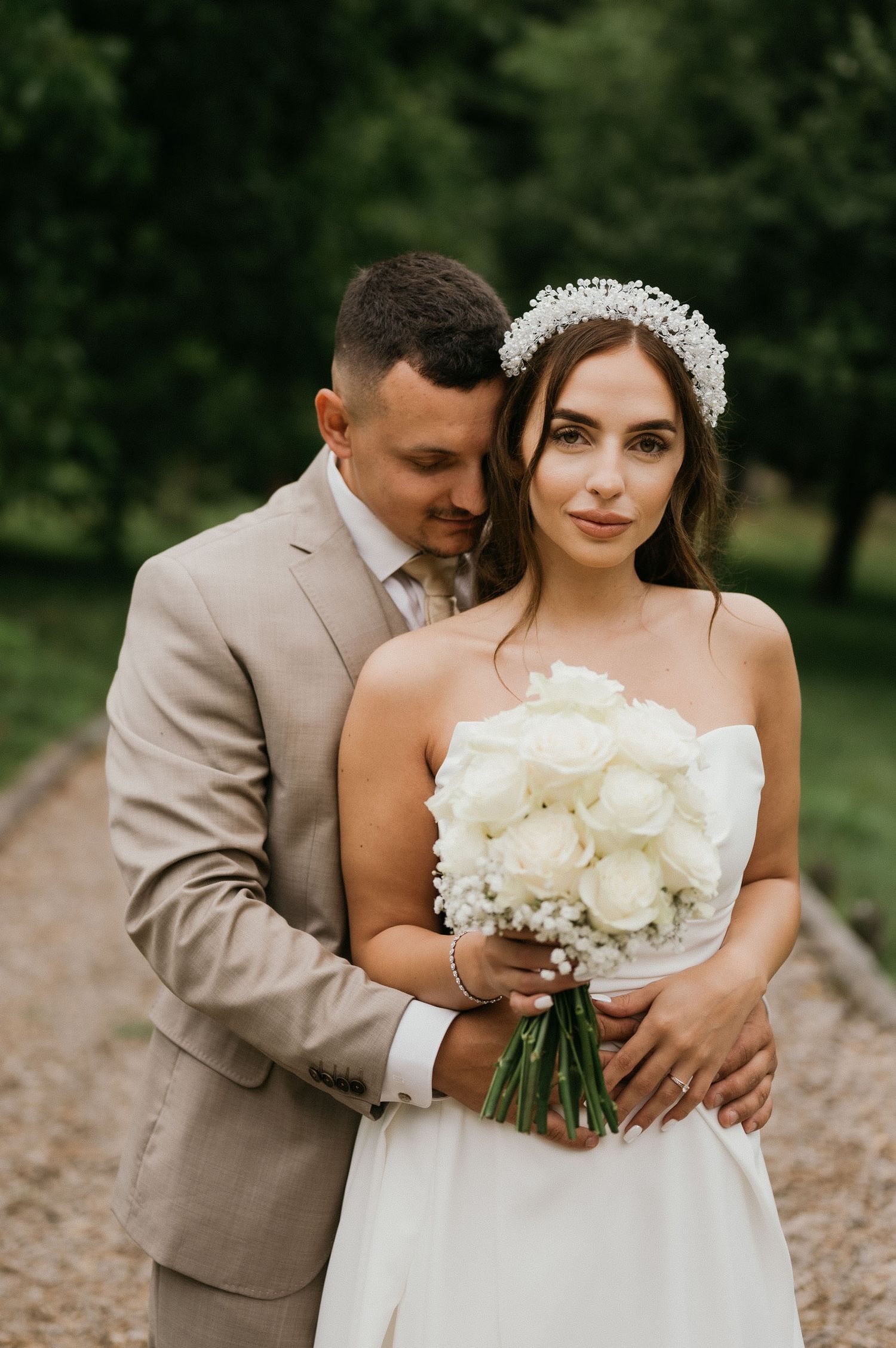 An intimate wedding portrait featuring a beige suit and white bridal gown with floral bouquet.