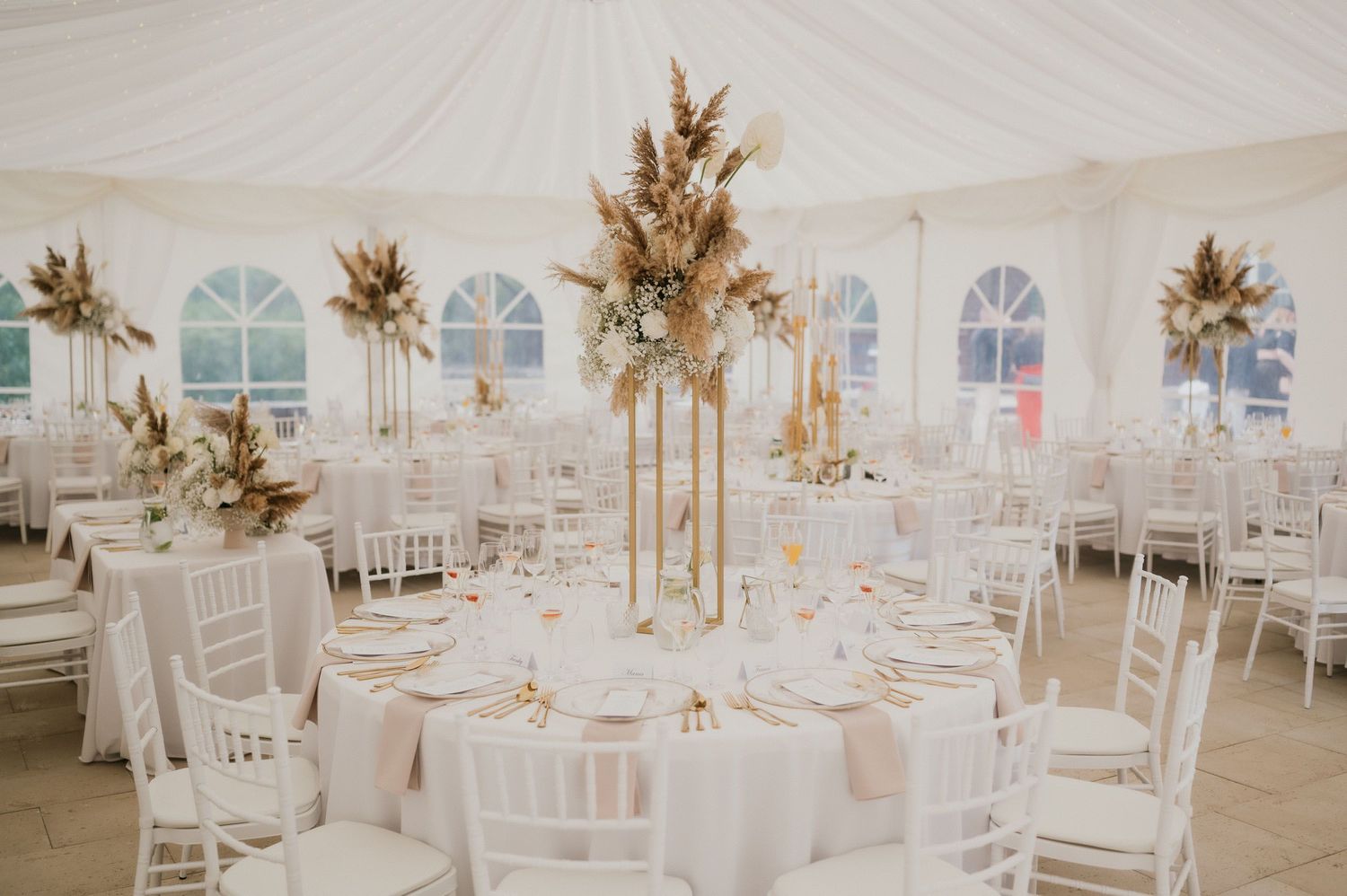 An ethereal wedding reception space with tall dried floral centerpieces and white decor.