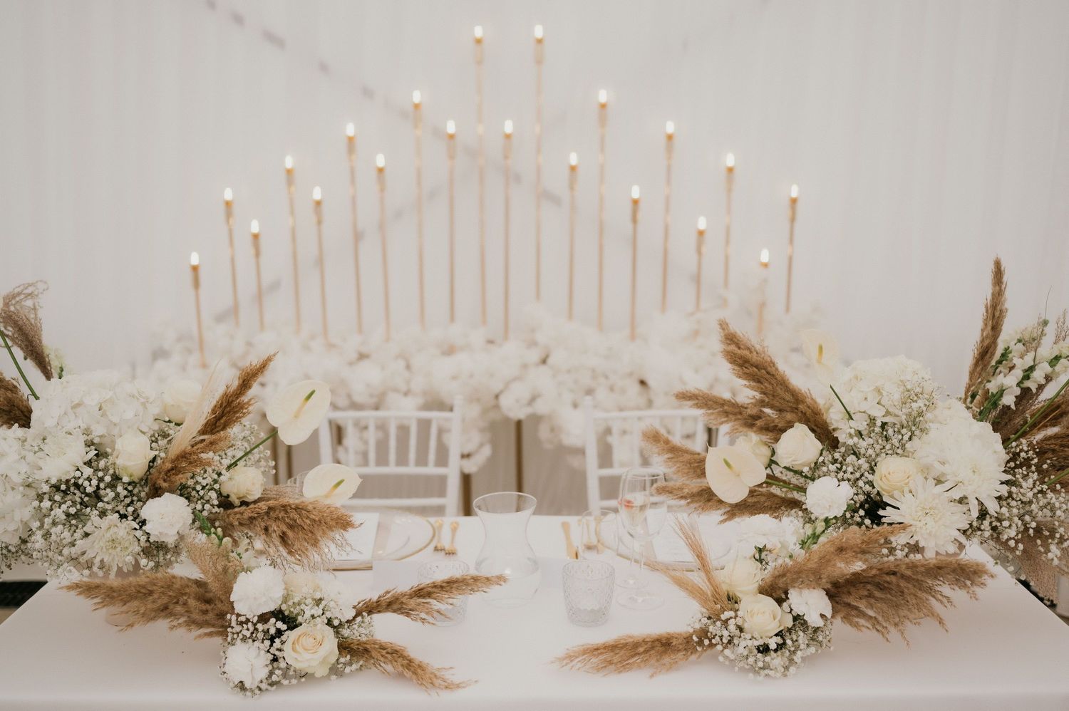 Modern wedding altar display with tall white candles and dried pampas grass floral arrangements.