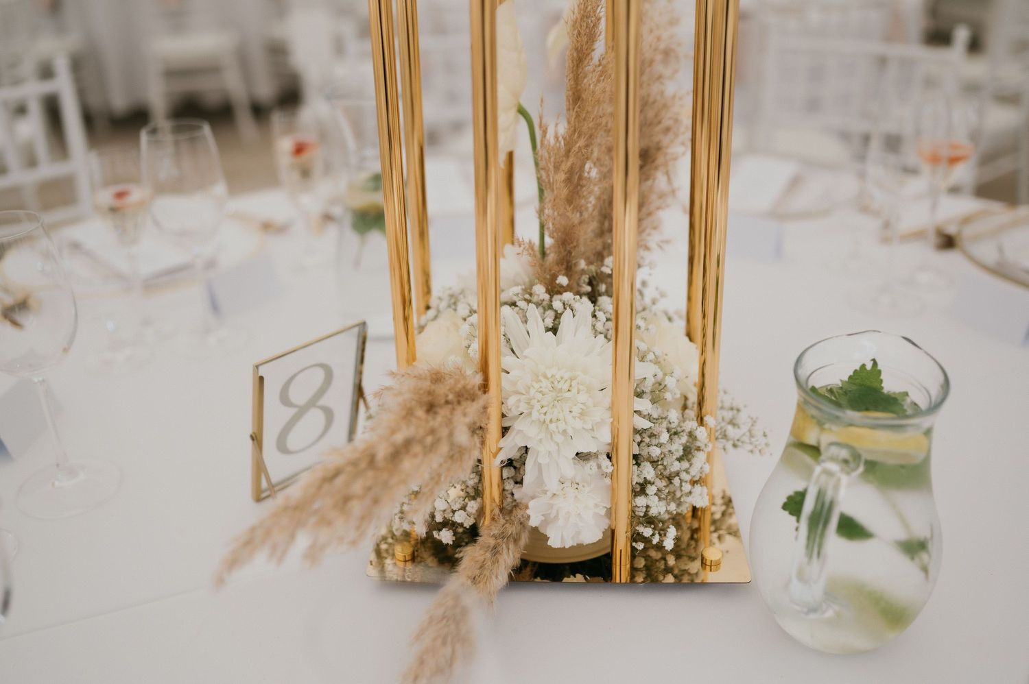 Wedding table centerpiece featuring gold candlesticks, baby's breath flowers and dried pampas grass.