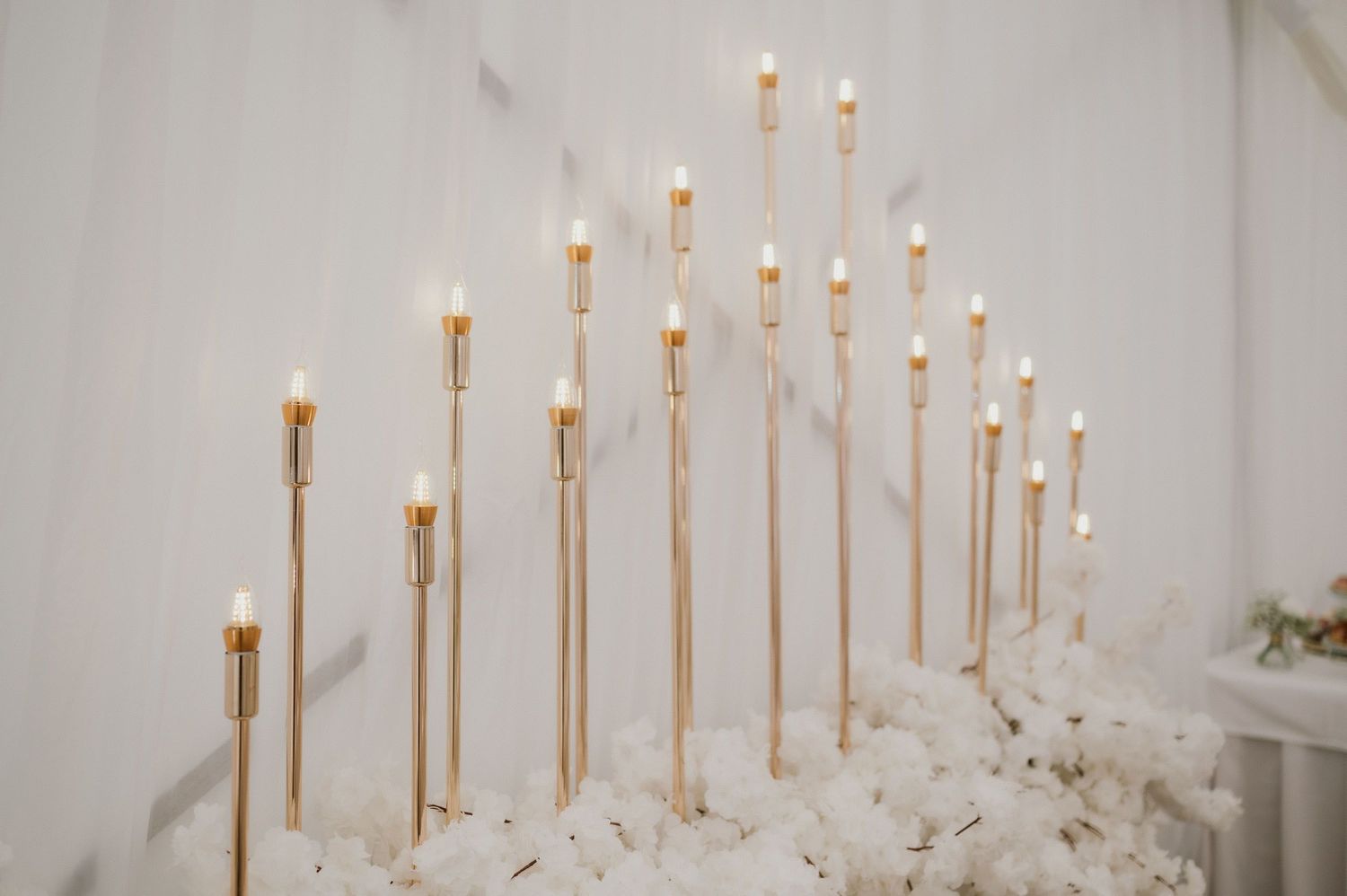 Minimalist wedding backdrop with cascading gold candlesticks on white textured base.