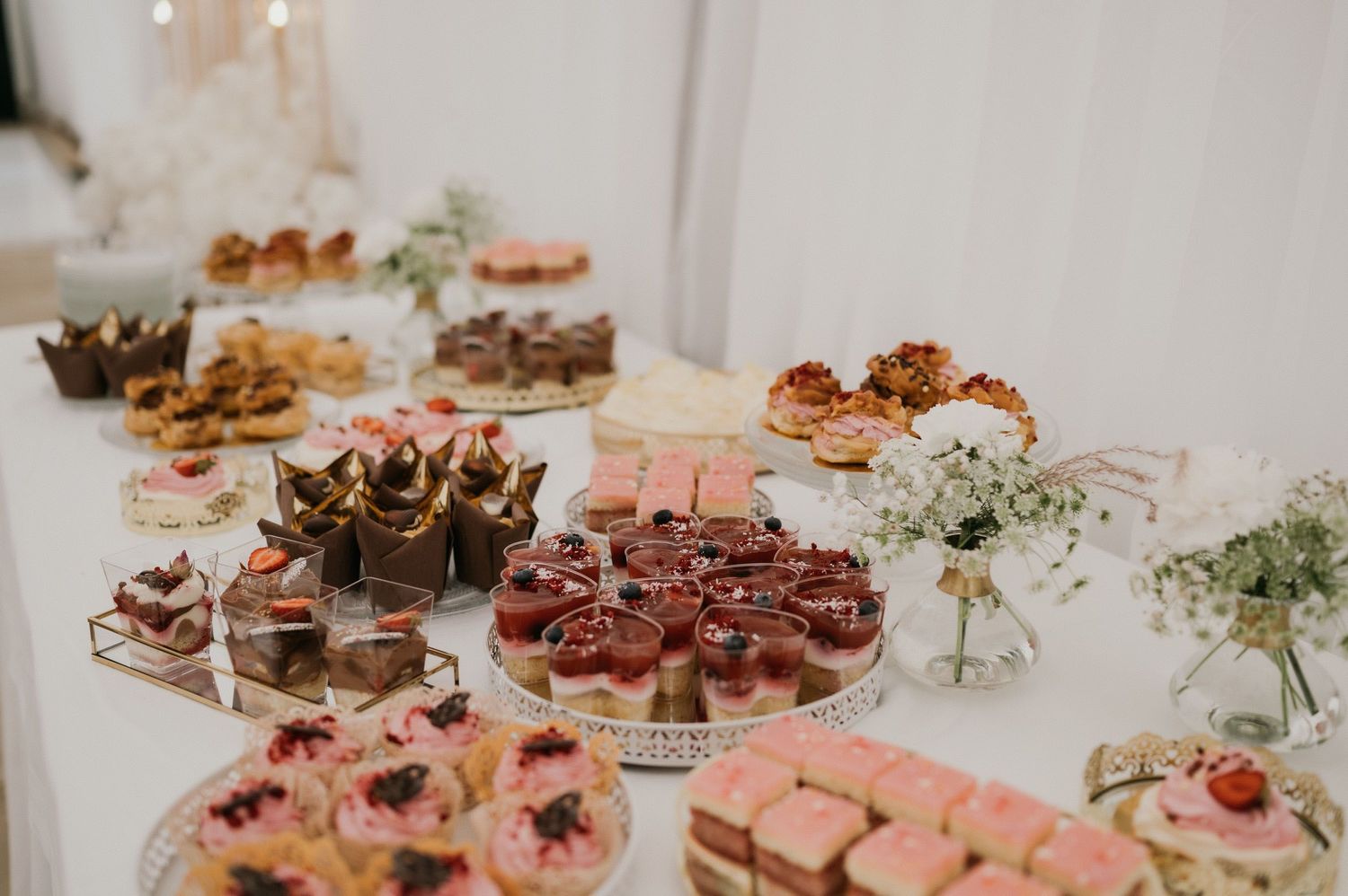 Elegant dessert table with variety of mini pastries and sweets at wedding reception.